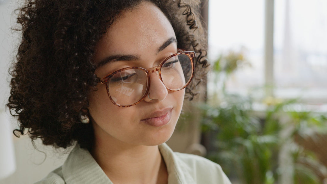 Close-up portrait of a woman with curly hair and eyeglasses indoors.