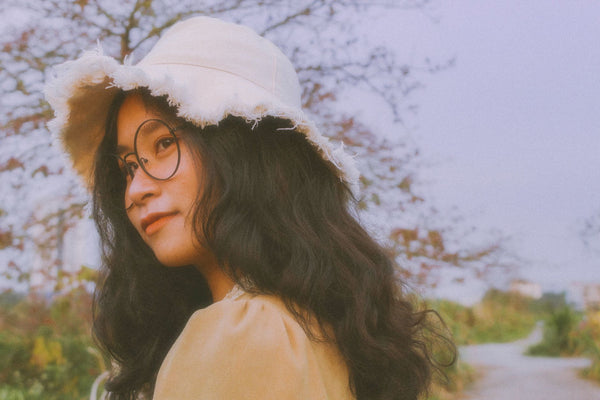 A serene portrait of a woman in a bucket hat and glasses, captured outdoors with natural light.