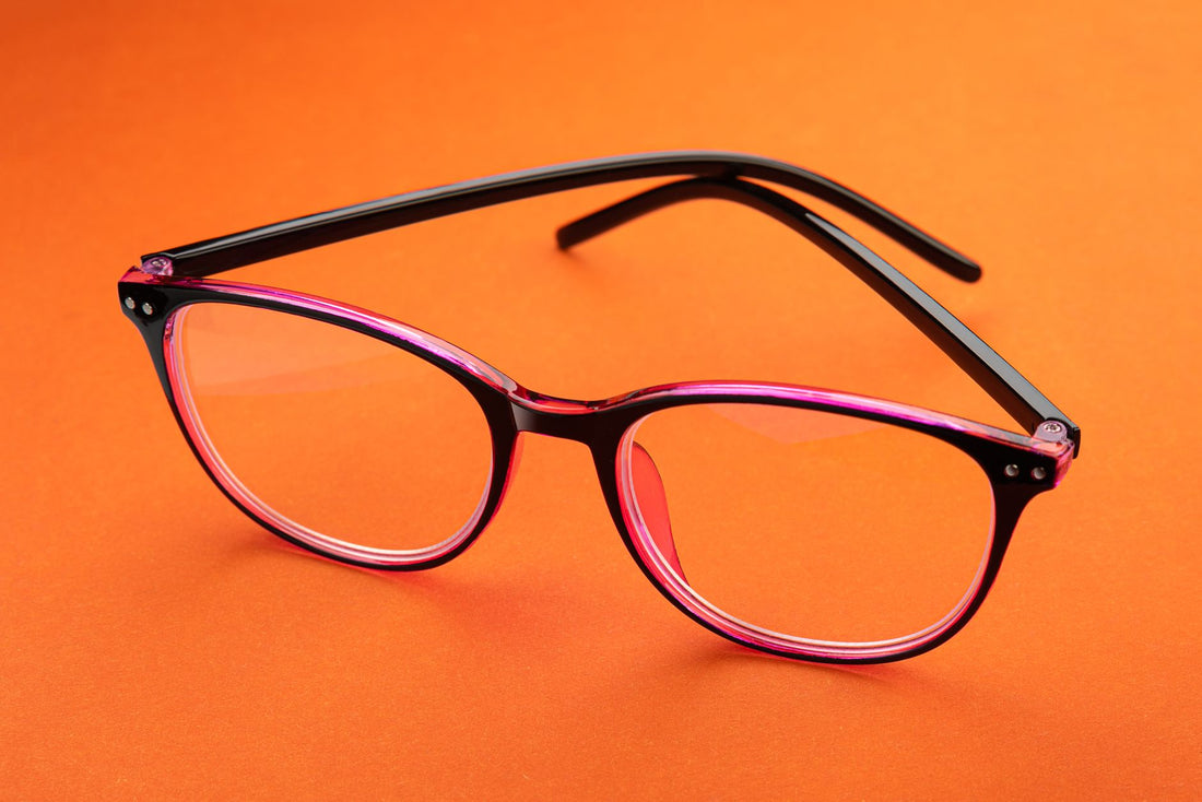 Close-up of pink eyeglasses resting on a bright orange surface. Perfect for eyewear fashion concepts.