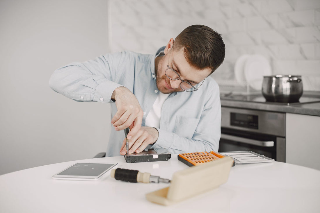 Man wearing glasses using a screwdriver to fix a device on a kitchen table.