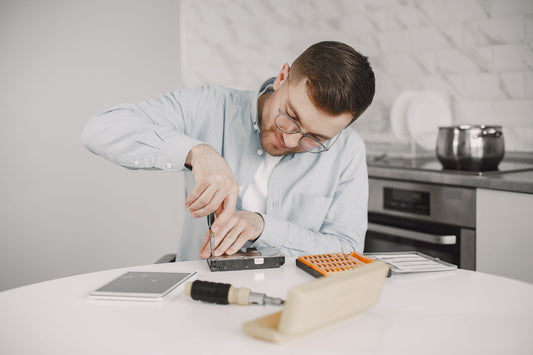 Man wearing glasses using a screwdriver to fix a device on a kitchen table.