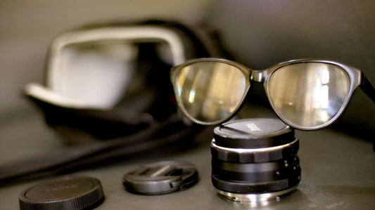 Closeup glasses in black rim on black photography lens placed on black table in front of photo bag