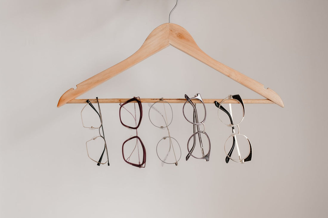 Various eyeglasses frames neatly hanging on a wooden clothes hanger with neutral background.
