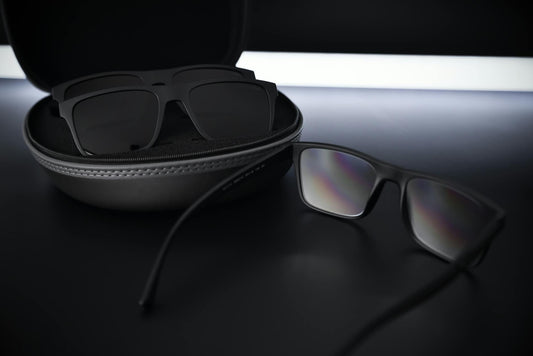 Close-up of black sunglasses and case on a reflective, sleek surface.
