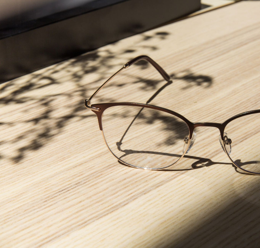 Close-up of stylish eyeglasses casting a shadow on a sunlit wooden table.