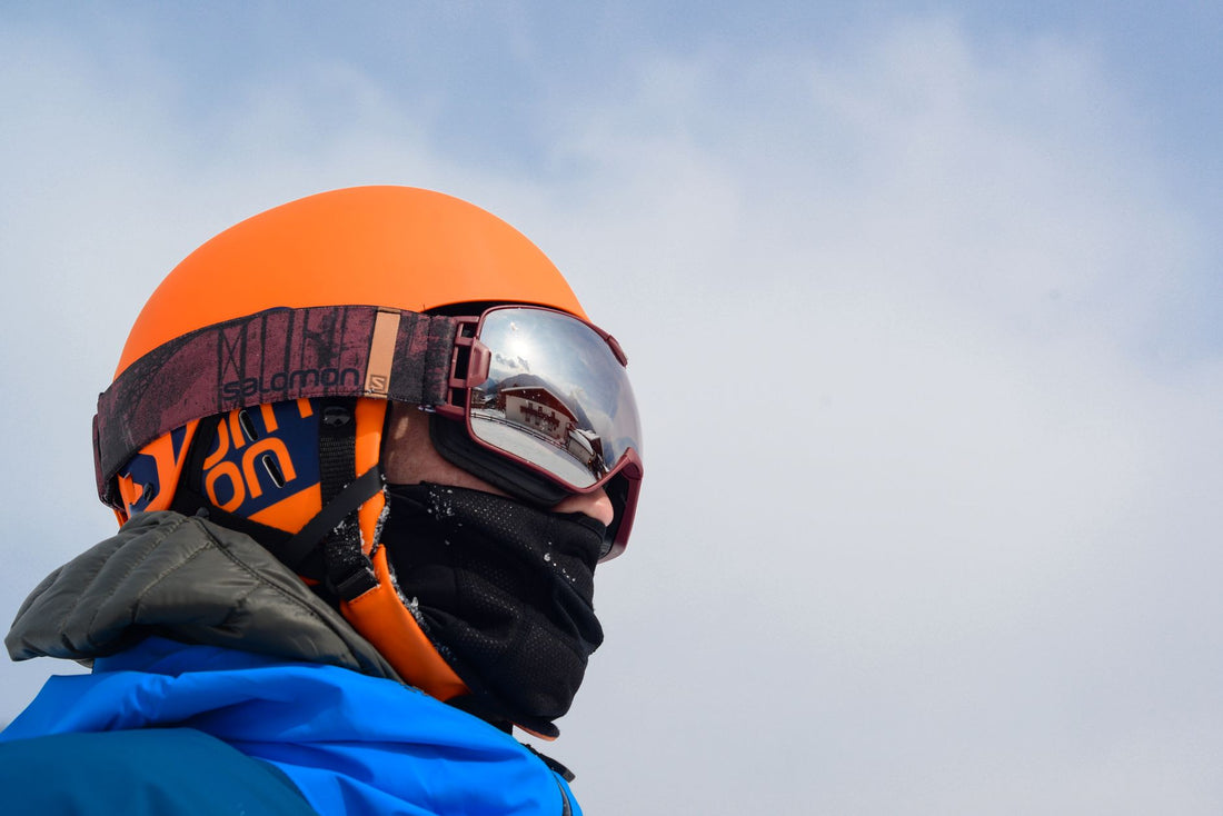 Close-up of a man wearing winter sports gear and reflective goggles against a cloudy sky.